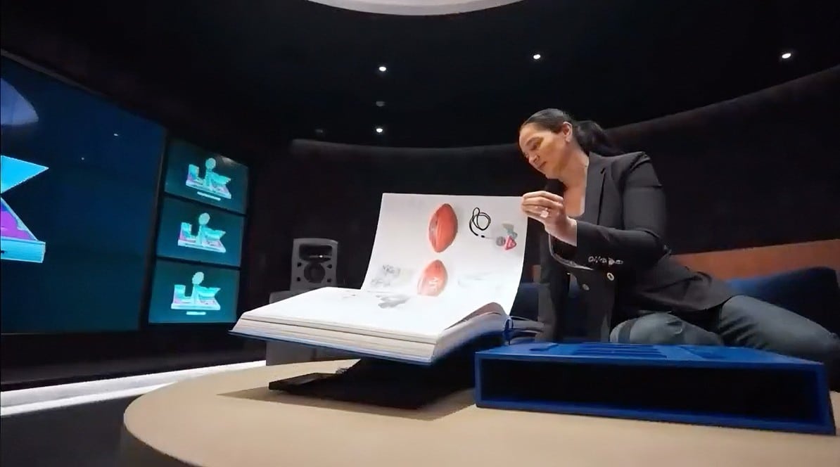 Desiree Perez sitting on a couch and carefully flipping through the pages of a large presentation book on a low table.